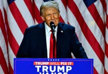 Trump regresa a la Casa Blanca: El sorprendente triunfo que sacudió a América Donald Trump sonríe con confianza en un podio con un cartel que dice 'Trump Will Fix It' y 'Trump Vance', con una bandera estadounidense de fondo, simbolizando el triunfo de Trump y su continuo apoyo político.