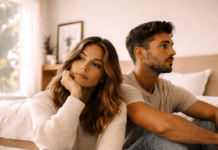 3 desventajas de ser la pareja “fácil” Pareja hispana sentada en el suelo de una habitación iluminada por luz natural, con expresión pensativa y distancia emocional, representando la desconexión en relaciones y las desventajas de ser la pareja “fácil”, incluyendo dificultad para expresar emociones, evitar conflictos, ansiedad en la relación y falta de comunicación en pareja.